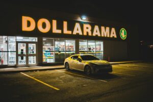 Expensive contemporary car placed on asphalt road near shop with large and bright signboard at night
